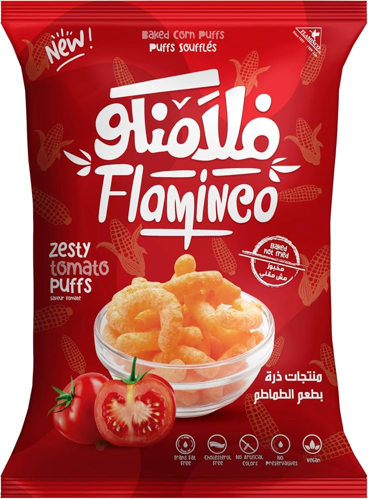 A red bag of Flaminco Zesty Tomato Puffs, featuring a bowl of golden-orange puffs and fresh tomato graphics on the front, with the brand name 'Flaminco' prominently displayed in white Arabic script.
